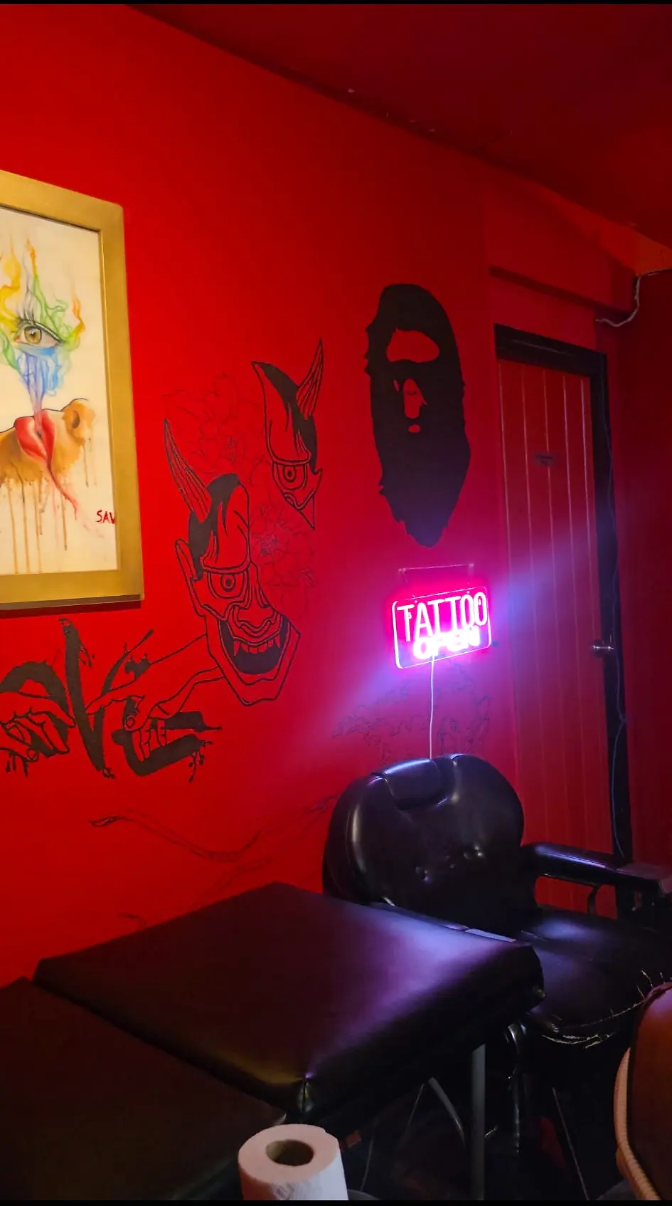 The red studio's tattoo chair beneath hand-painted murals and a neon sign