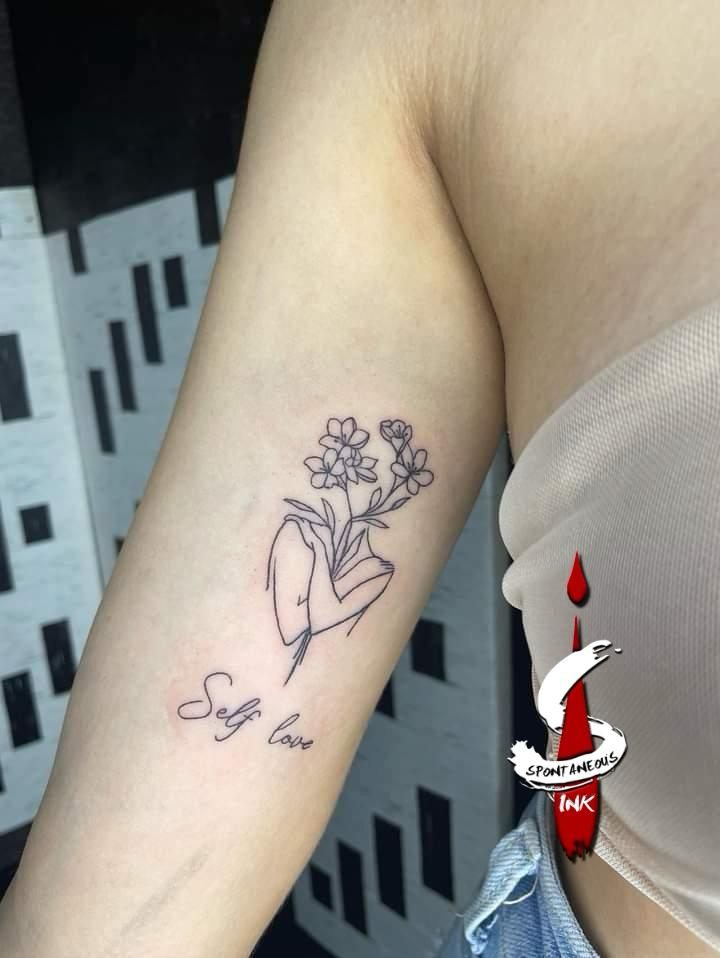 Fine-line hand holding flowers with Self love script, upper arm