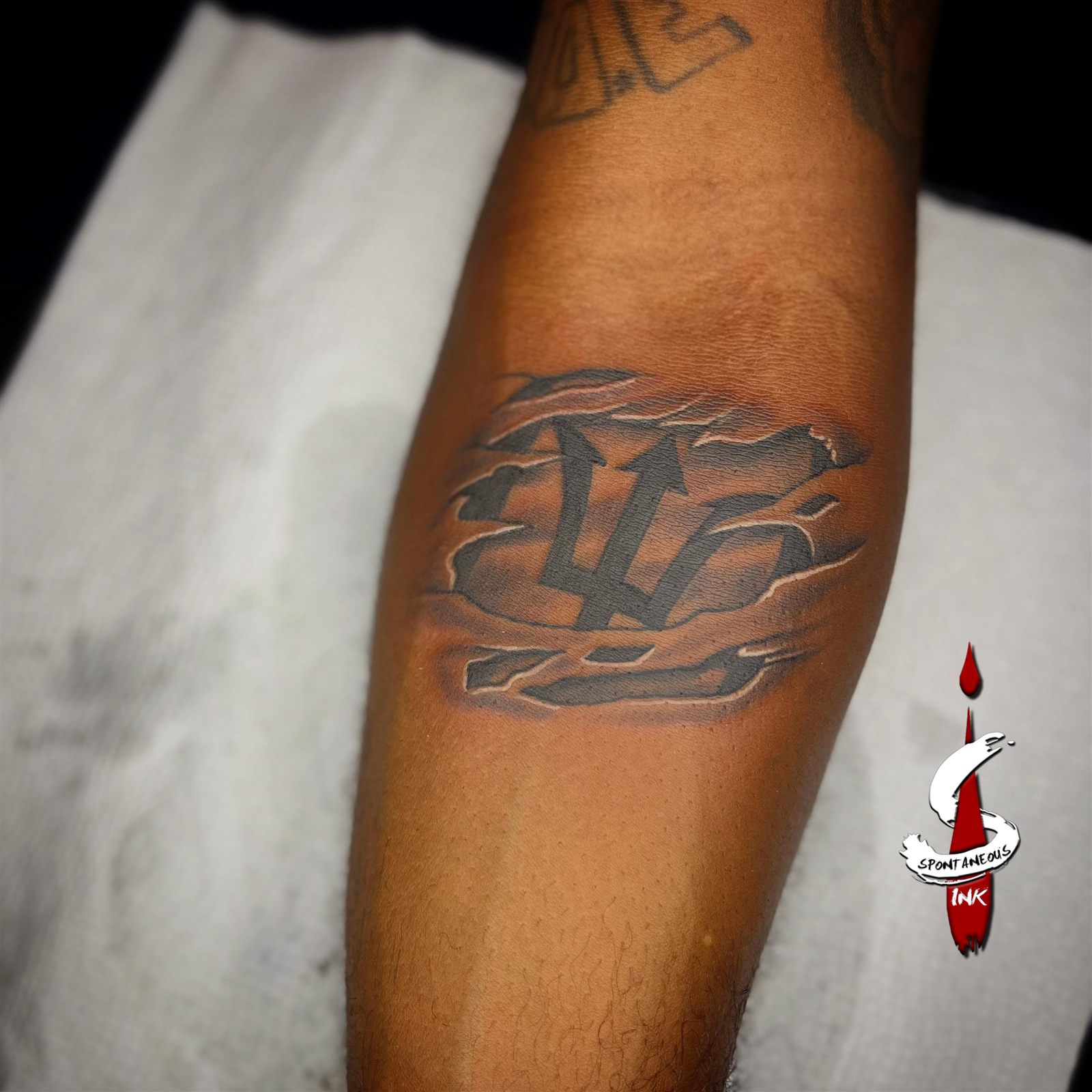 Barbados trident rendered as torn skin, black and grey, forearm