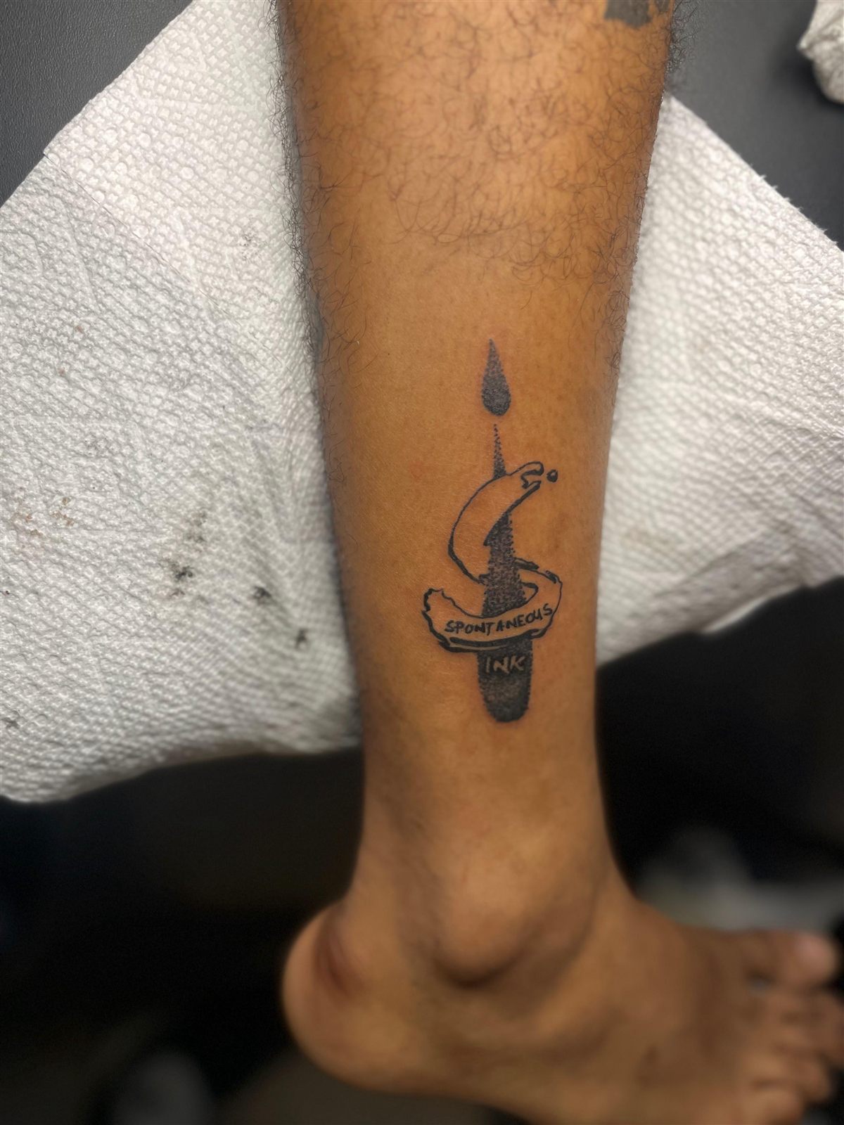 A client tattooed with the Spontaneous Ink logo on the lower leg